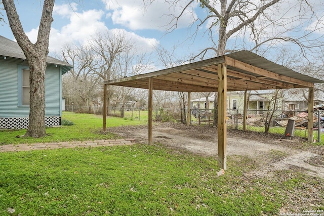 view of yard featuring dirt driveway, fence, and a carport