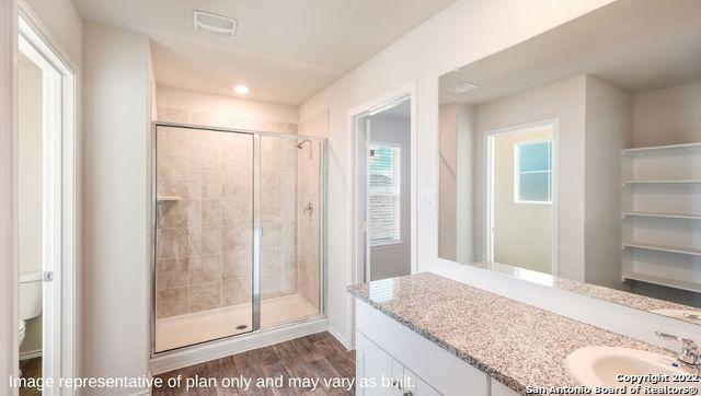 full bath with a stall shower, visible vents, wood finished floors, and vanity