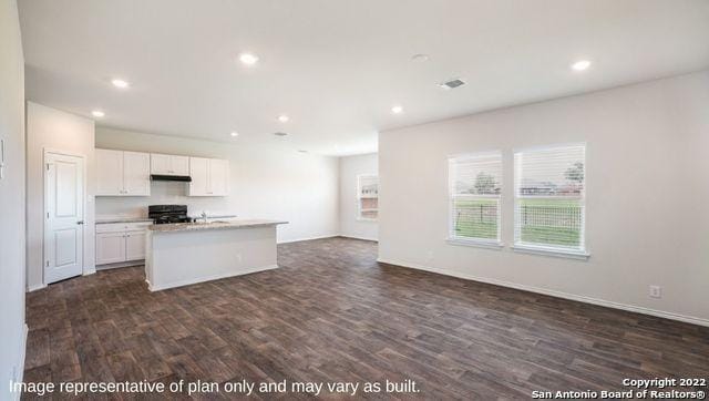 kitchen with range, an island with sink, open floor plan, under cabinet range hood, and white cabinetry