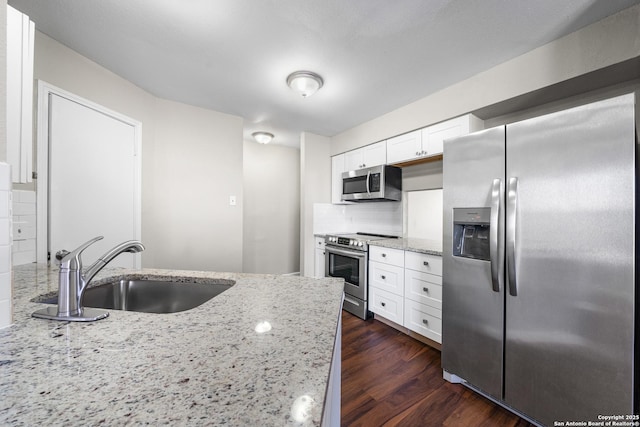 kitchen featuring decorative backsplash, white cabinets, appliances with stainless steel finishes, light stone countertops, and a sink