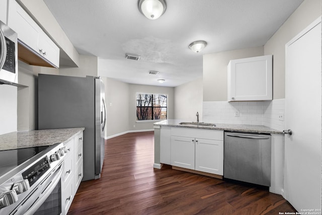 kitchen with a sink, white cabinetry, appliances with stainless steel finishes, light stone countertops, and dark wood-style floors