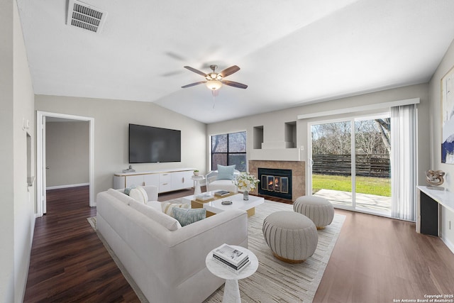 living room featuring dark wood finished floors, visible vents, vaulted ceiling, a ceiling fan, and a glass covered fireplace