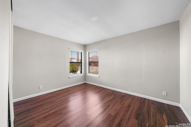 spare room featuring dark wood-style floors and baseboards