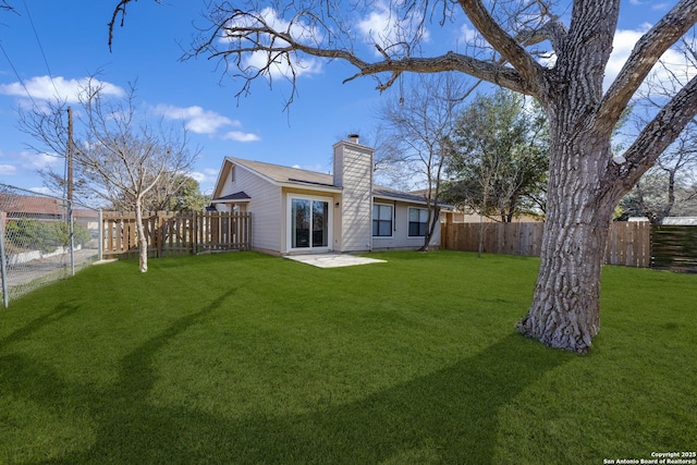 back of property with a patio area, a fenced backyard, a chimney, and a yard