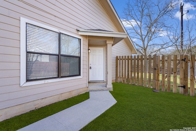 view of exterior entry with a yard and fence