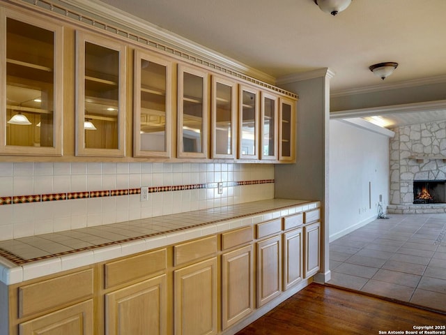 kitchen featuring open floor plan, ornamental molding, tile counters, tasteful backsplash, and glass insert cabinets