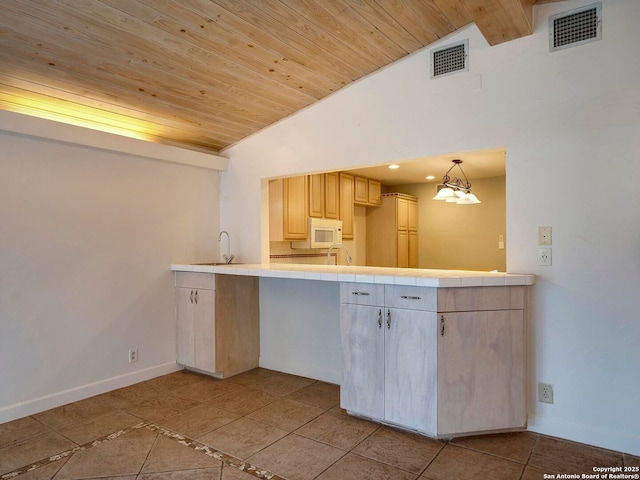 kitchen with lofted ceiling, hanging light fixtures, white microwave, and visible vents