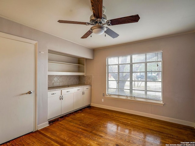 interior space with ornamental molding, dark wood finished floors, a ceiling fan, and baseboards