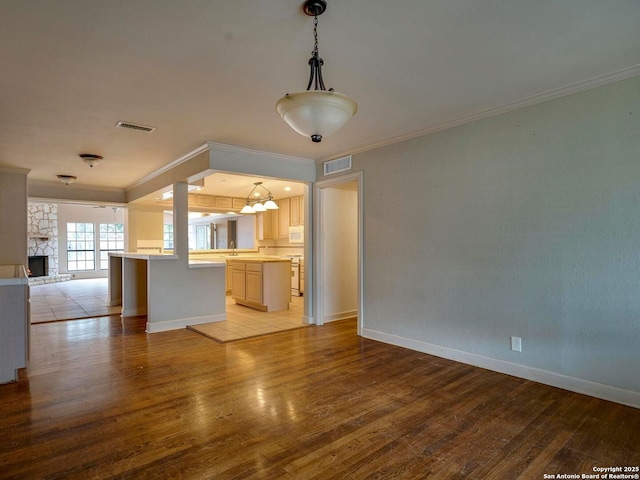 kitchen with pendant lighting, light countertops, ornamental molding, open floor plan, and light wood-type flooring