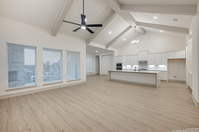 kitchen featuring white cabinets, open floor plan, a kitchen island with sink, light countertops, and high vaulted ceiling