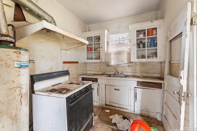 kitchen with white gas range oven, glass insert cabinets, light countertops, and a sink