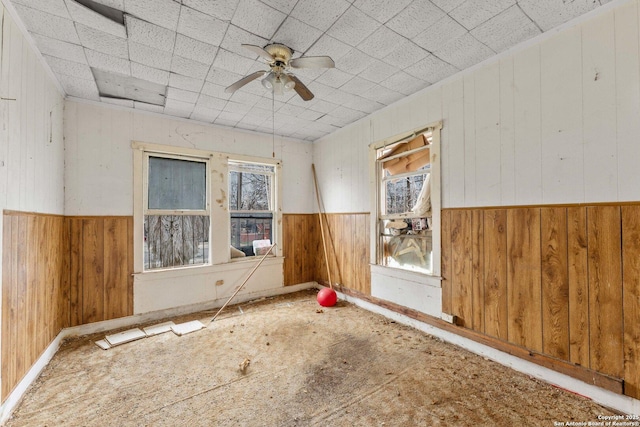 spare room with a ceiling fan, a wainscoted wall, and wood walls