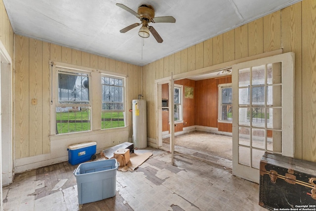 unfurnished room featuring water heater, ceiling fan, french doors, and wood walls