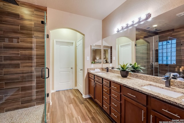 bathroom with double vanity, wood finished floors, a sink, and a shower stall