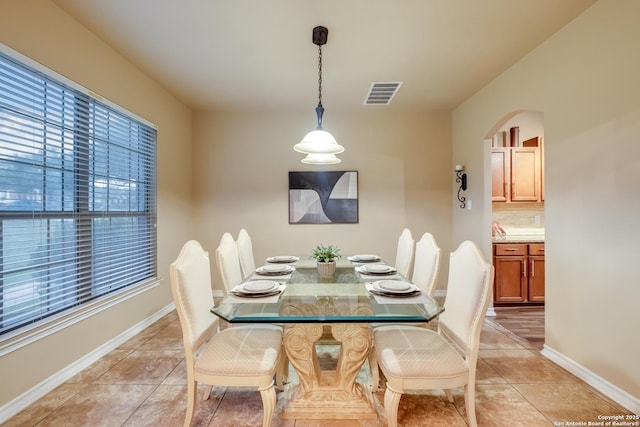 dining area with light tile patterned floors, baseboards, visible vents, and arched walkways