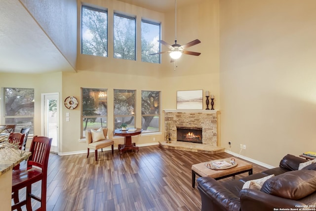 living room with a warm lit fireplace, ceiling fan, baseboards, and wood finished floors