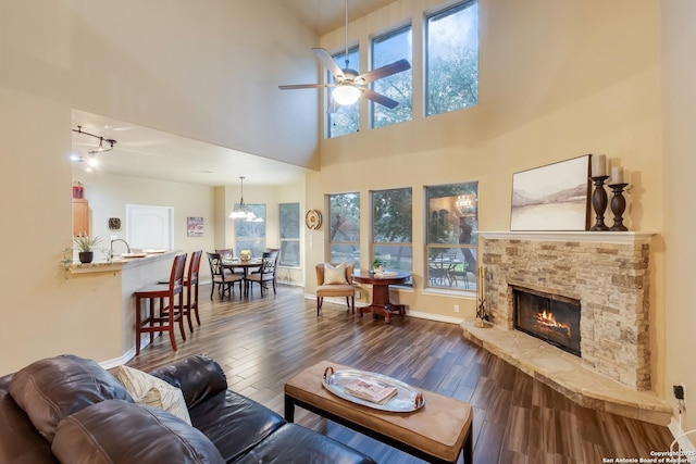 living area featuring ceiling fan, a fireplace, baseboards, and dark wood-style flooring