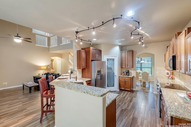 kitchen featuring arched walkways, stainless steel appliances, open floor plan, and brown cabinetry