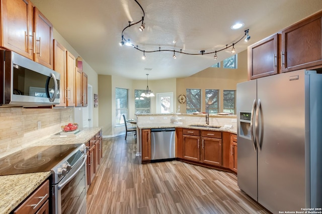 kitchen with stainless steel appliances, hanging light fixtures, a sink, and brown cabinets