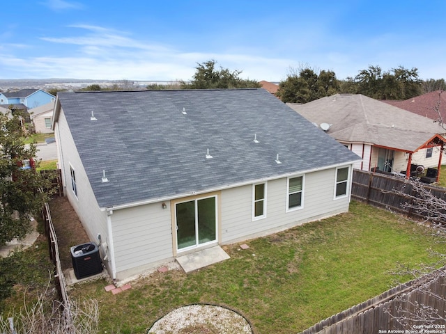 rear view of property with a fenced backyard, central AC unit, a lawn, and roof with shingles