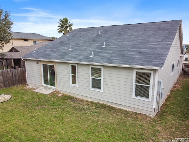 back of house with a shingled roof, a yard, and fence