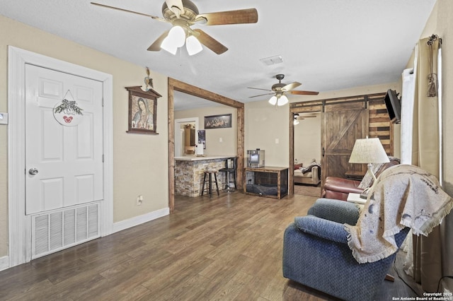 living area with wood finished floors, visible vents, ceiling fan, and a barn door