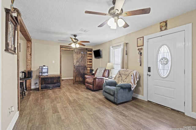 entryway with light wood-style floors, ceiling fan, a textured ceiling, and a barn door