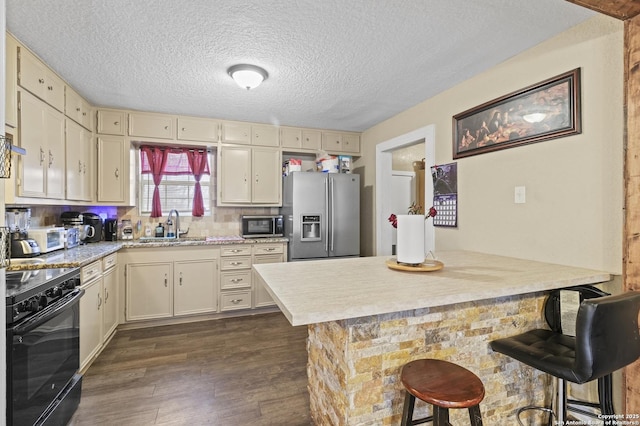 kitchen featuring light countertops, appliances with stainless steel finishes, cream cabinetry, and a kitchen breakfast bar