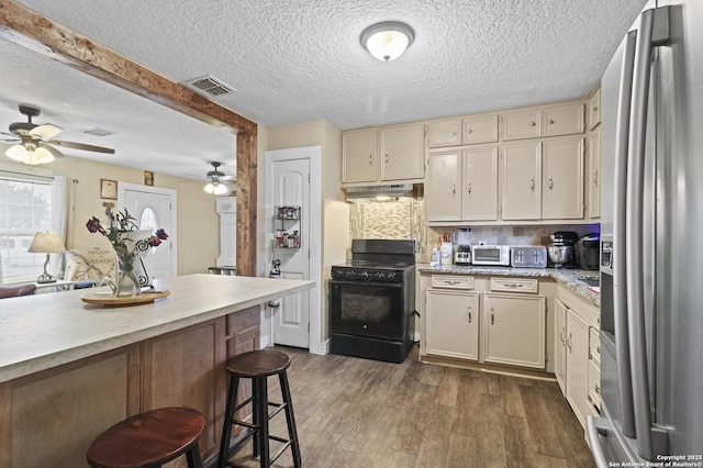 kitchen with cream cabinetry, light countertops, black range with gas stovetop, stainless steel fridge, and under cabinet range hood