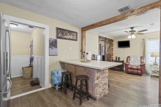 kitchen featuring a kitchen bar, visible vents, a barn door, wood finished floors, and stainless steel fridge with ice dispenser