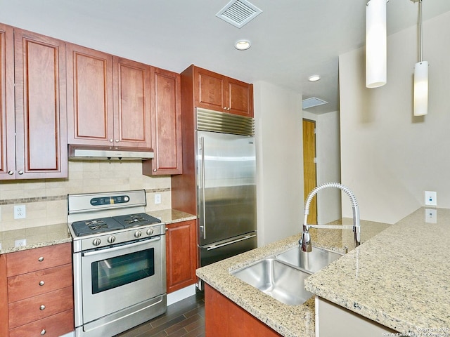 kitchen with under cabinet range hood, a sink, appliances with stainless steel finishes, light stone countertops, and pendant lighting