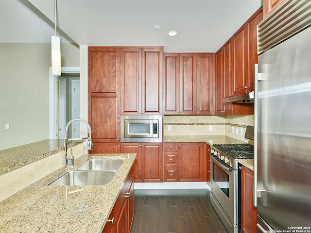 kitchen featuring light stone counters, hanging light fixtures, stainless steel appliances, under cabinet range hood, and a sink