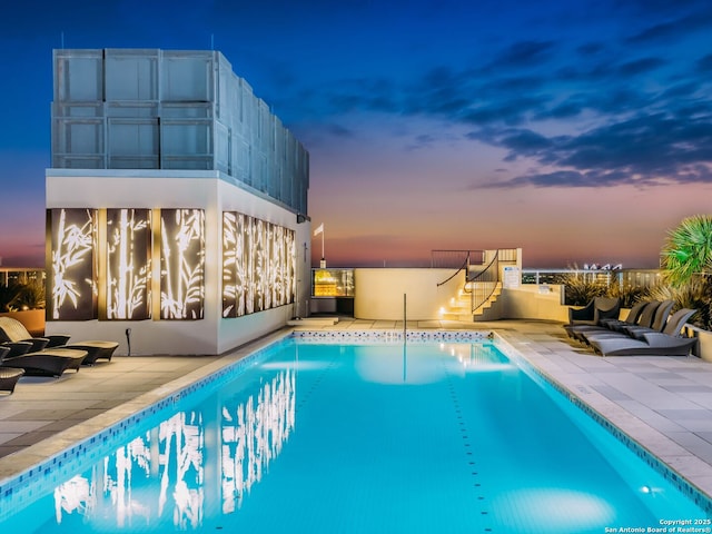 pool at dusk featuring a patio area, stairway, and a community pool