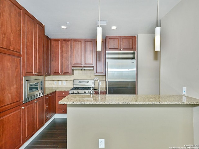 kitchen featuring visible vents, built in appliances, hanging light fixtures, light stone countertops, and under cabinet range hood