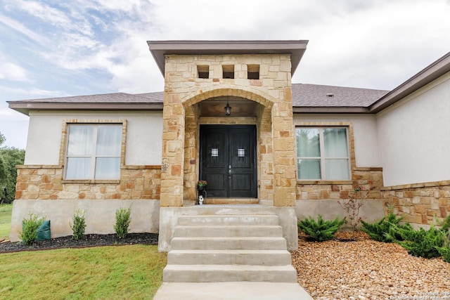 view of exterior entry featuring stone siding, roof with shingles, and stucco siding