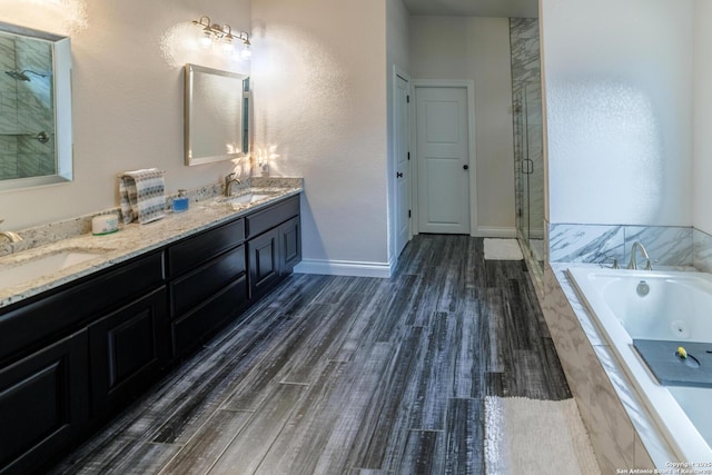 full bathroom featuring wood finished floors, a sink, a jetted tub, double vanity, and a stall shower