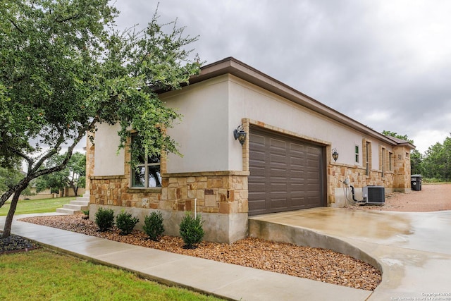 view of side of home featuring central air condition unit, stucco siding, concrete driveway, a garage, and stone siding