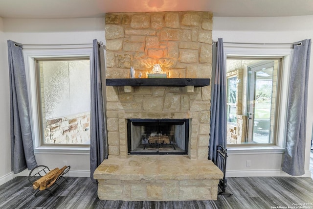 room details featuring a stone fireplace, baseboards, and wood finished floors