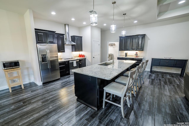 kitchen with stainless steel appliances, a sink, visible vents, wall chimney range hood, and a center island with sink