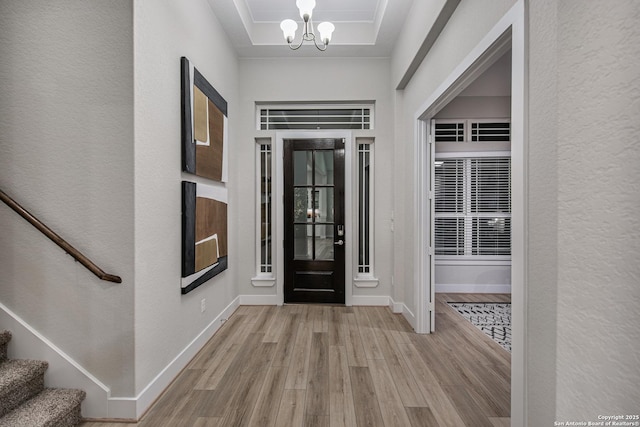 foyer entrance featuring a notable chandelier, a raised ceiling, light wood-style floors, baseboards, and stairs