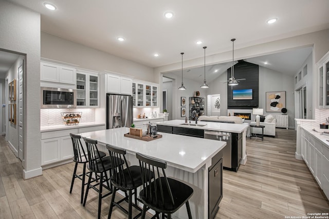 kitchen featuring open floor plan, light countertops, appliances with stainless steel finishes, a center island with sink, and glass insert cabinets