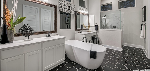 bathroom with a walk in shower, two vanities, a sink, baseboards, and a soaking tub