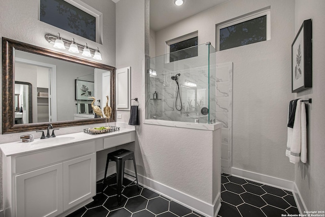 bathroom featuring a walk in shower, a textured wall, vanity, baseboards, and tile patterned floors