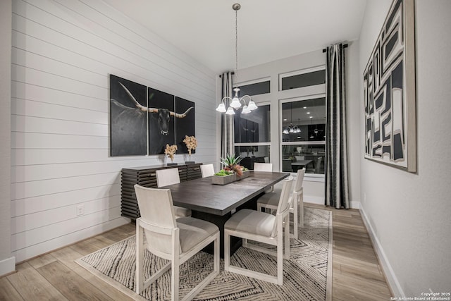 dining room featuring a notable chandelier, wood walls, baseboards, and light wood-style floors