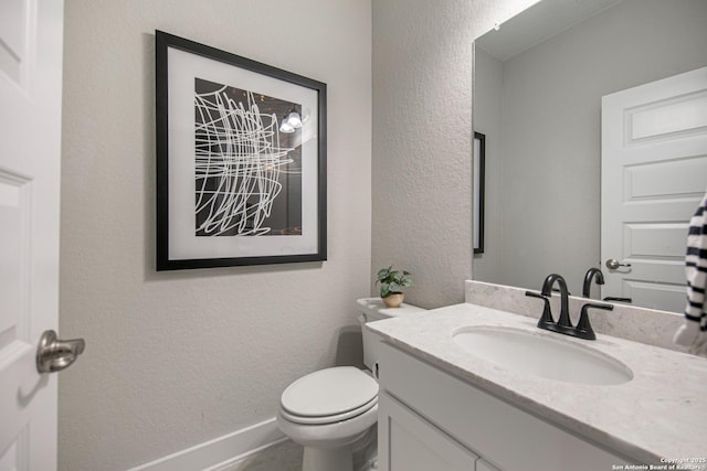 bathroom featuring baseboards, a textured wall, vanity, and toilet