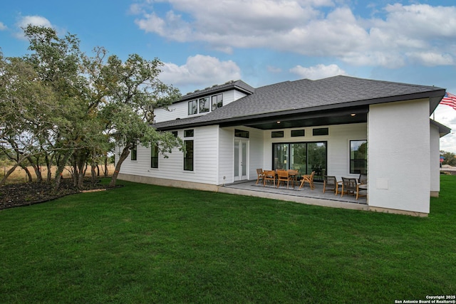 rear view of house featuring roof with shingles, a patio, and a yard