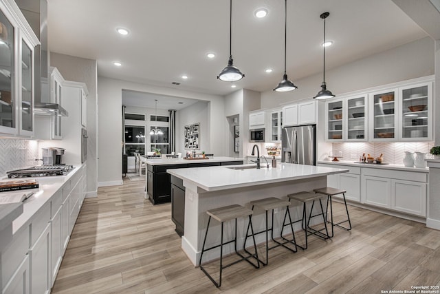 kitchen with decorative light fixtures, light countertops, appliances with stainless steel finishes, glass insert cabinets, and a kitchen island with sink