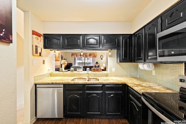 kitchen with stainless steel appliances, dark cabinetry, a sink, and dark wood-type flooring