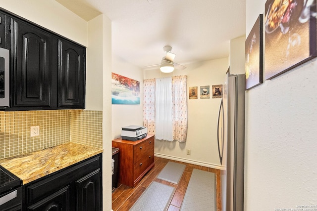 kitchen featuring ceiling fan, dark cabinets, dark wood-style flooring, freestanding refrigerator, and decorative backsplash