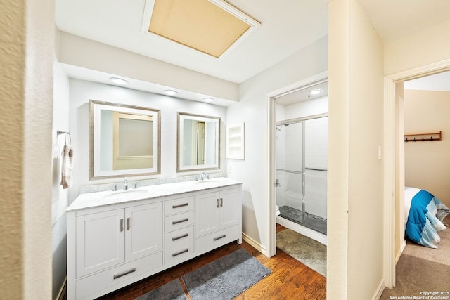 bathroom featuring double vanity, a stall shower, a sink, and wood finished floors